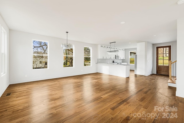 unfurnished living room with sink, wood-type flooring, and an inviting chandelier