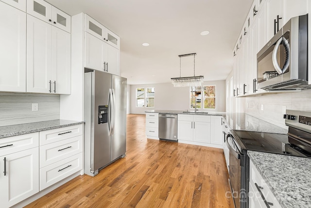 kitchen with white cabinets, stainless steel appliances, hanging light fixtures, and light hardwood / wood-style flooring