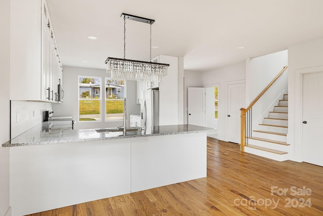 kitchen with hardwood / wood-style floors, stainless steel fridge with ice dispenser, decorative light fixtures, light stone counters, and white cabinetry