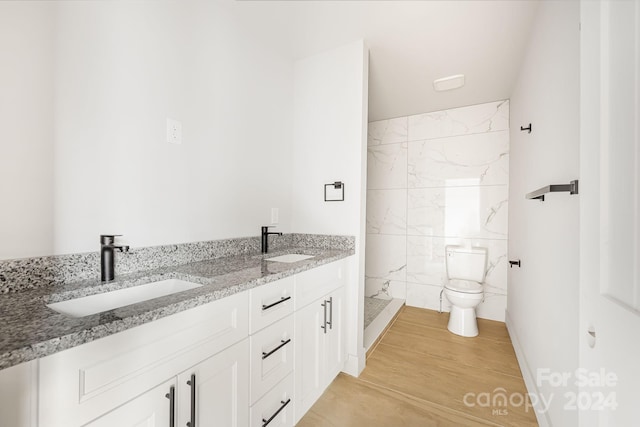 bathroom featuring hardwood / wood-style floors, vanity, toilet, and tiled shower