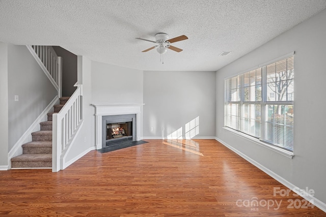 unfurnished living room featuring ceiling fan, hardwood / wood-style floors, and a textured ceiling