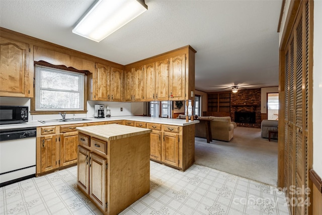 kitchen with sink, kitchen peninsula, white dishwasher, a fireplace, and a kitchen island