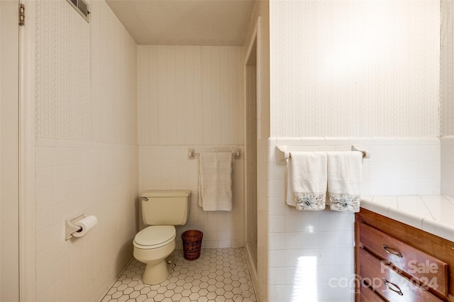 bathroom featuring tile patterned floors, vanity, toilet, and tile walls