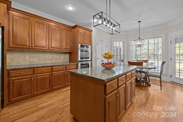 kitchen with stainless steel double oven, dark stone countertops, pendant lighting, light hardwood / wood-style floors, and a kitchen island