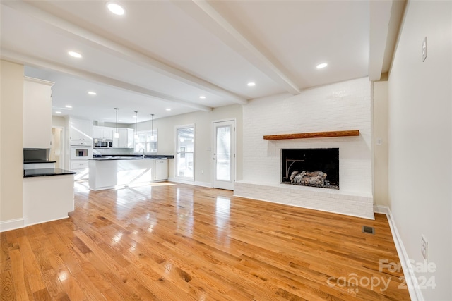 unfurnished living room with beam ceiling, a fireplace, and light wood-type flooring