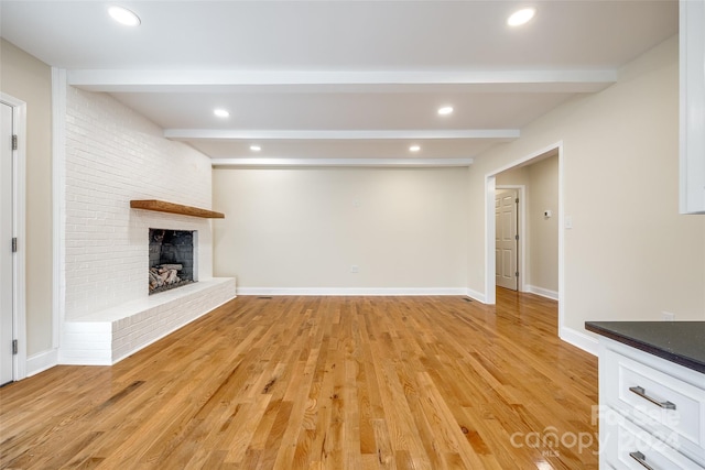 unfurnished living room featuring beamed ceiling, a brick fireplace, and light hardwood / wood-style flooring