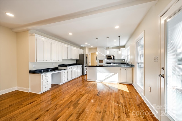 kitchen with white cabinets, hanging light fixtures, appliances with stainless steel finishes, and light hardwood / wood-style flooring