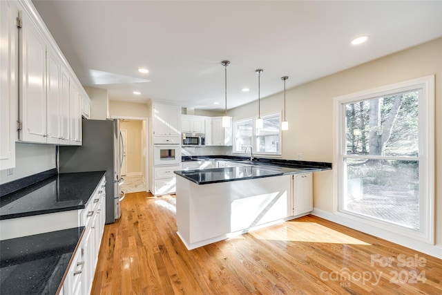 kitchen featuring white cabinets, hanging light fixtures, light wood-type flooring, kitchen peninsula, and stainless steel appliances