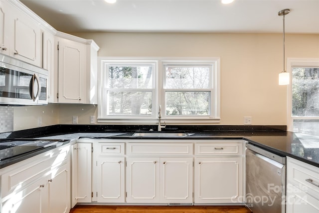 kitchen with stainless steel appliances, sink, dark stone countertops, white cabinetry, and hanging light fixtures