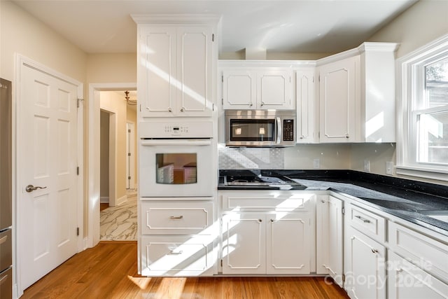 kitchen with white cabinets, light hardwood / wood-style floors, backsplash, and appliances with stainless steel finishes