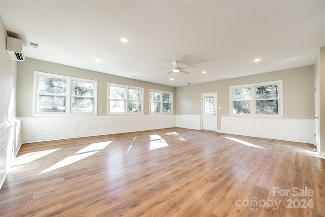 unfurnished room featuring a wall unit AC, ceiling fan, brick wall, and hardwood / wood-style flooring