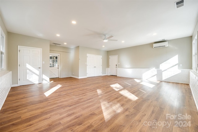 unfurnished living room featuring ceiling fan, light hardwood / wood-style floors, and a wall mounted air conditioner