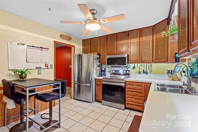 kitchen with appliances with stainless steel finishes, light tile patterned floors, ceiling fan, and sink