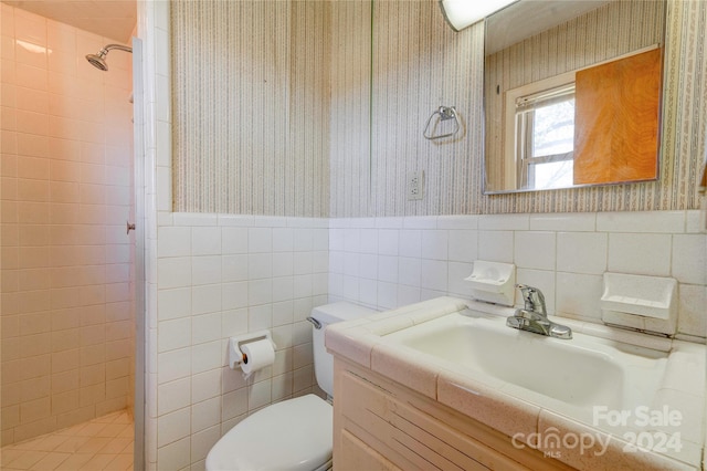 bathroom with vanity, toilet, a tile shower, and tile walls