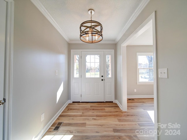 foyer entrance with ornamental molding, a textured ceiling, light hardwood / wood-style floors, and a notable chandelier