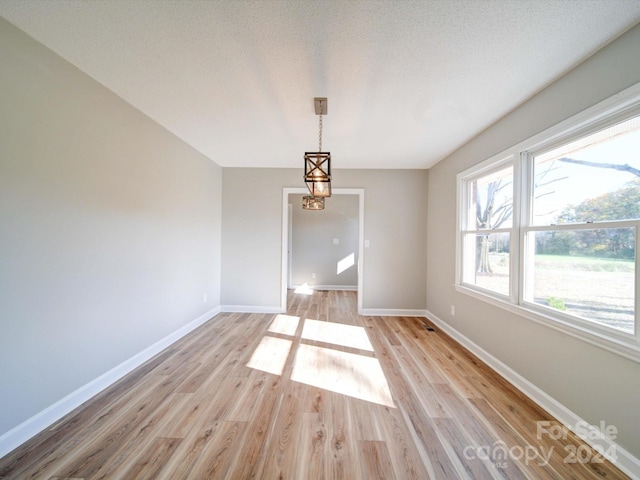 unfurnished dining area with a textured ceiling and light wood-type flooring