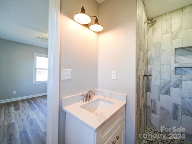 bathroom with hardwood / wood-style floors, vanity, and a tile shower