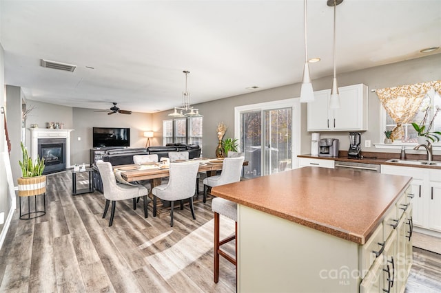 kitchen with ceiling fan, sink, white cabinets, a kitchen island, and light wood-type flooring