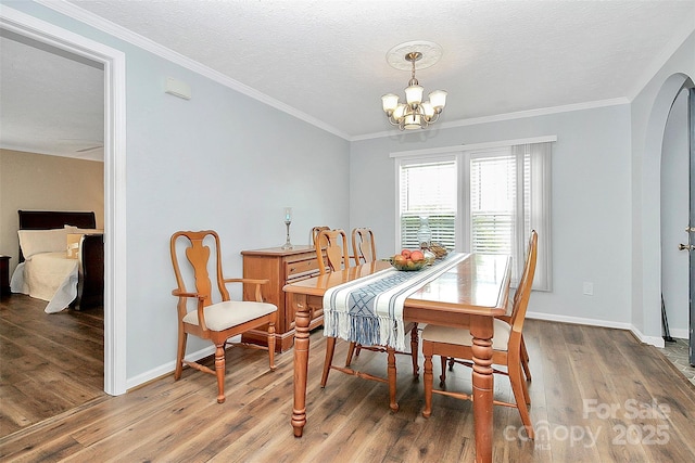 dining space featuring arched walkways, crown molding, wood finished floors, and an inviting chandelier