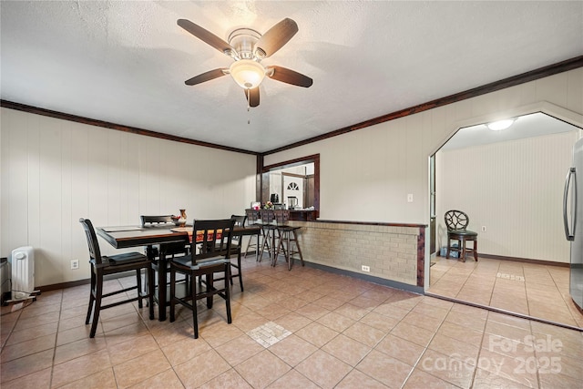 tiled dining area featuring a textured ceiling, ornamental molding, ceiling fan, and wood walls