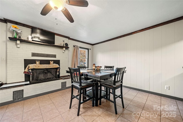 dining room featuring wooden walls, a textured ceiling, light tile patterned flooring, ceiling fan, and ornamental molding