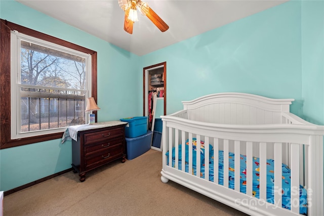 carpeted bedroom featuring ceiling fan and a nursery area