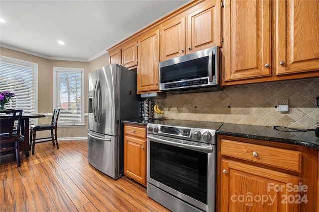 kitchen featuring stainless steel appliances, light hardwood / wood-style flooring, dark stone countertops, decorative backsplash, and ornamental molding