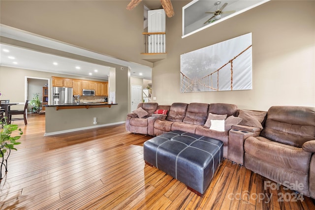 living room featuring ceiling fan, light hardwood / wood-style floors, and a high ceiling