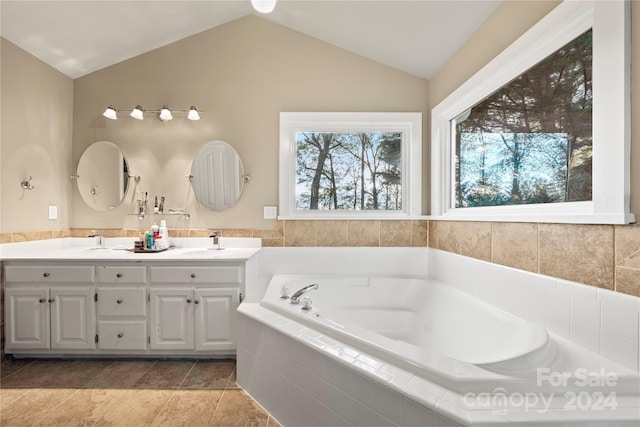 bathroom with vanity, tiled bath, and vaulted ceiling