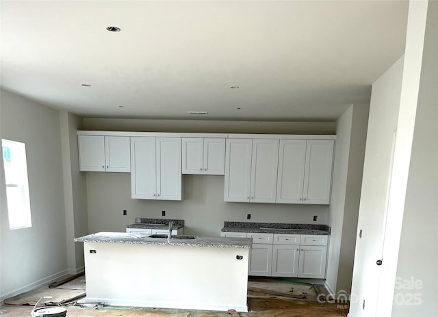 kitchen with white cabinets, stone countertops, sink, and an island with sink