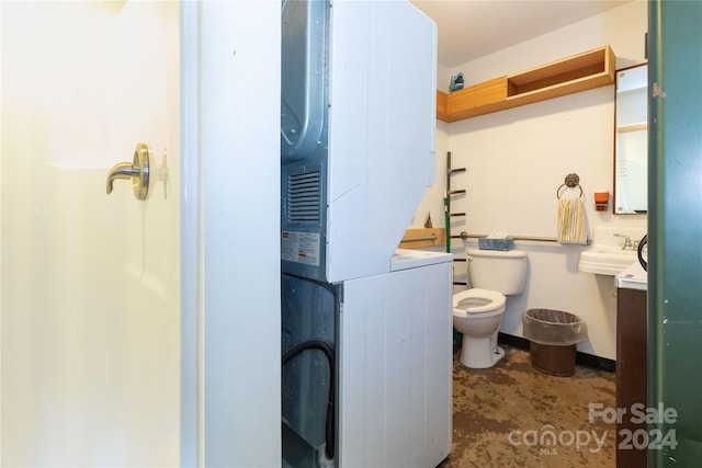 bathroom featuring sink, toilet, and stacked washer / dryer