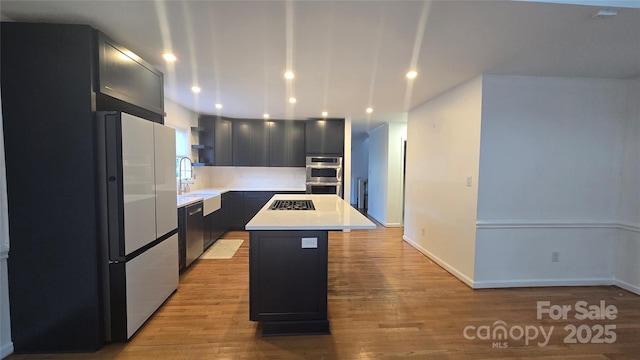 kitchen with light wood-type flooring, a sink, a kitchen island, appliances with stainless steel finishes, and light countertops