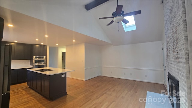 kitchen featuring beamed ceiling, light wood-style flooring, stainless steel double oven, a fireplace, and light countertops