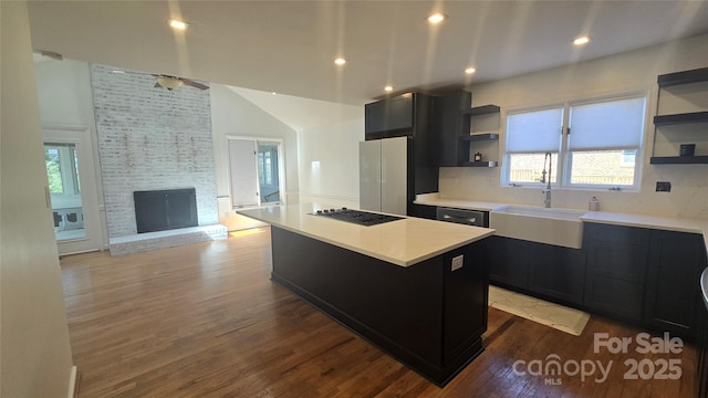 kitchen featuring gas cooktop, a kitchen island, open shelves, a sink, and dark cabinets