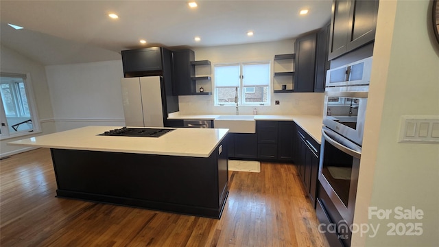 kitchen with gas cooktop, wood finished floors, a kitchen island, open shelves, and a sink