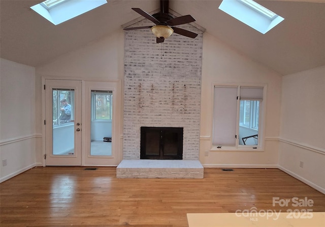 unfurnished living room with a brick fireplace, a skylight, wood finished floors, and visible vents