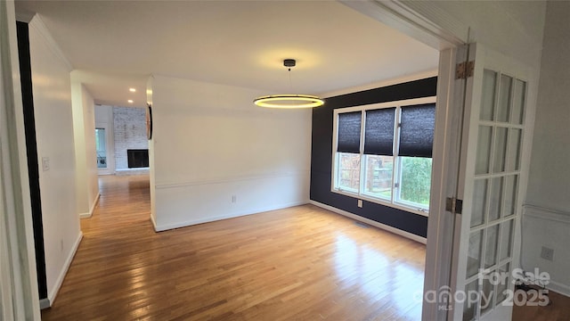 empty room featuring a fireplace, wood finished floors, visible vents, and baseboards