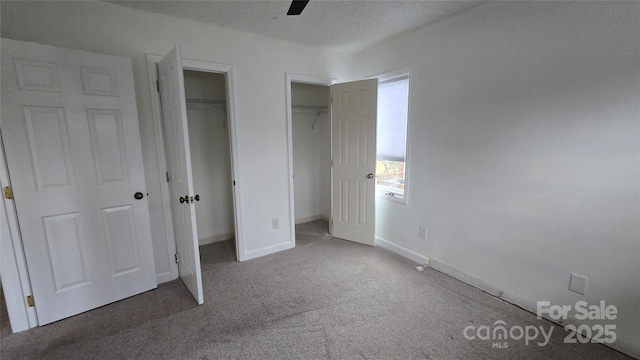 unfurnished bedroom featuring multiple closets, a textured ceiling, carpet, baseboards, and ceiling fan