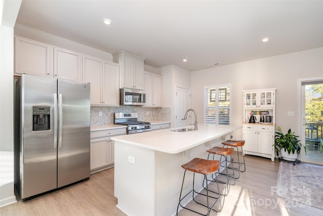 kitchen with a center island with sink, white cabinets, sink, light hardwood / wood-style floors, and stainless steel appliances