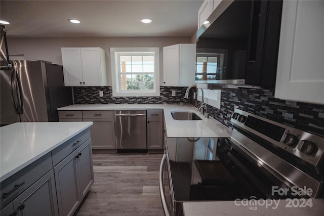 kitchen with appliances with stainless steel finishes, backsplash, sink, light hardwood / wood-style floors, and white cabinetry