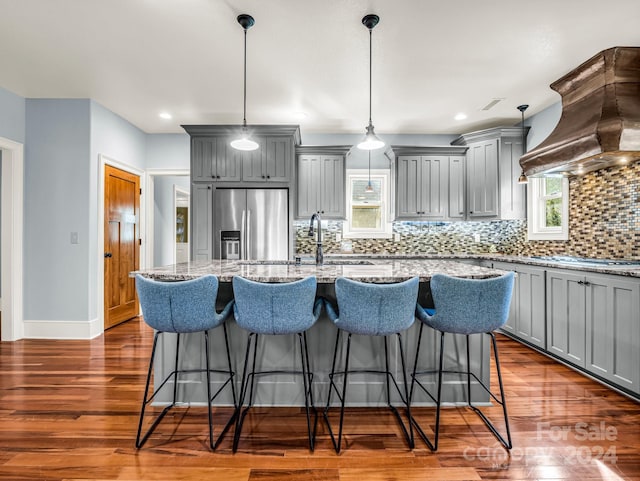 kitchen featuring custom exhaust hood, backsplash, appliances with stainless steel finishes, decorative light fixtures, and dark hardwood / wood-style flooring