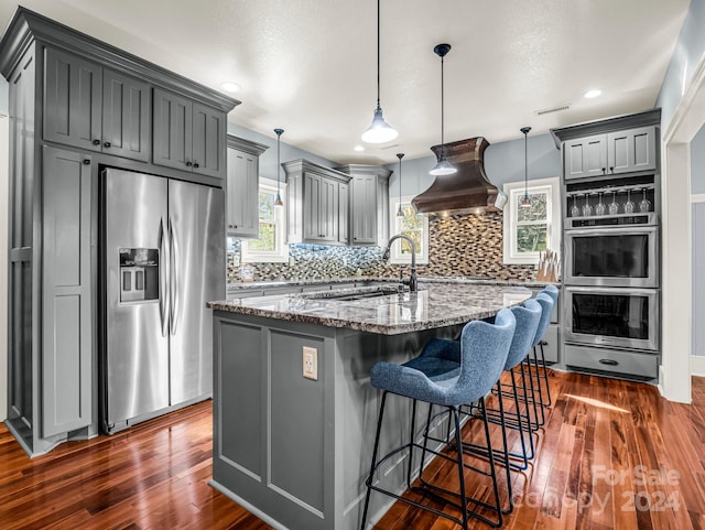 kitchen featuring dark hardwood / wood-style flooring, dark stone counters, gray cabinets, appliances with stainless steel finishes, and custom exhaust hood