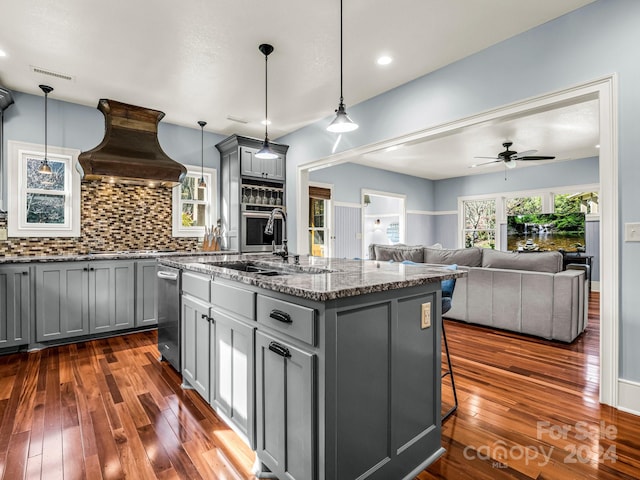 kitchen with custom range hood, dark hardwood / wood-style flooring, gray cabinets, and a center island with sink