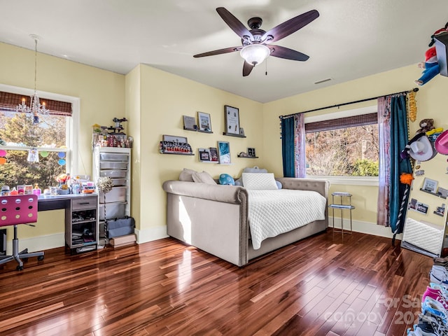 bedroom with wood-type flooring, ceiling fan with notable chandelier, and multiple windows