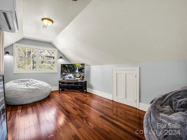 living area with a wall mounted air conditioner, a textured ceiling, dark hardwood / wood-style floors, and vaulted ceiling