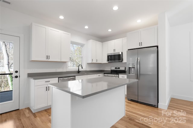 kitchen featuring light hardwood / wood-style flooring, appliances with stainless steel finishes, sink, white cabinetry, and a kitchen island