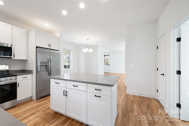 kitchen featuring appliances with stainless steel finishes, a center island, decorative light fixtures, white cabinetry, and light hardwood / wood-style flooring