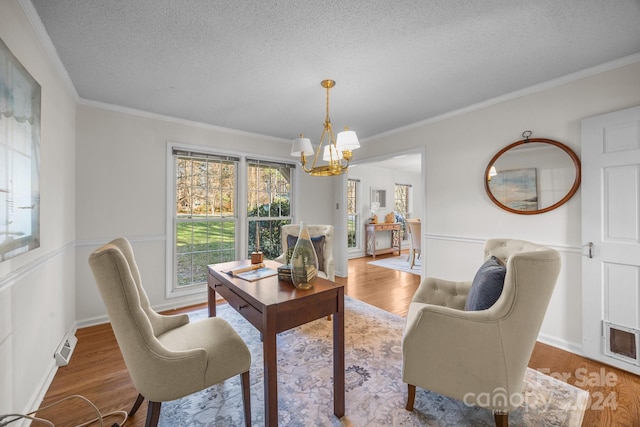 dining area featuring a chandelier, wood-type flooring, a textured ceiling, and ornamental molding