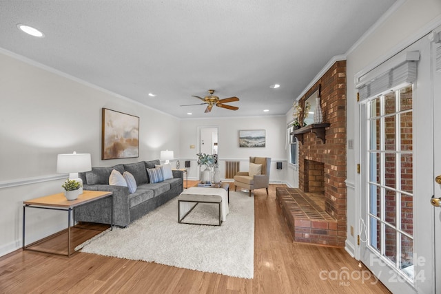 living room featuring light hardwood / wood-style flooring, ceiling fan, ornamental molding, a textured ceiling, and a fireplace