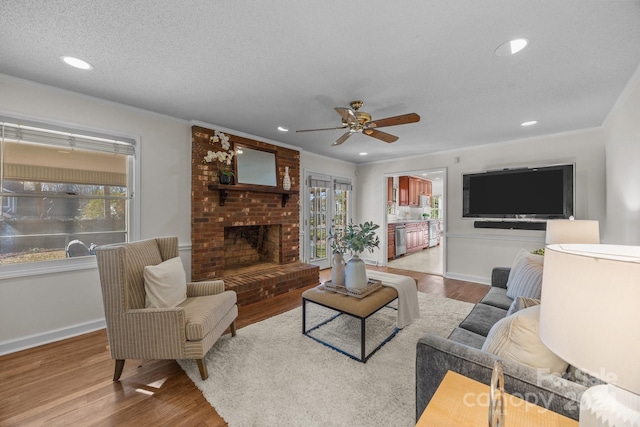 living room featuring ceiling fan, light hardwood / wood-style floors, a textured ceiling, and a brick fireplace